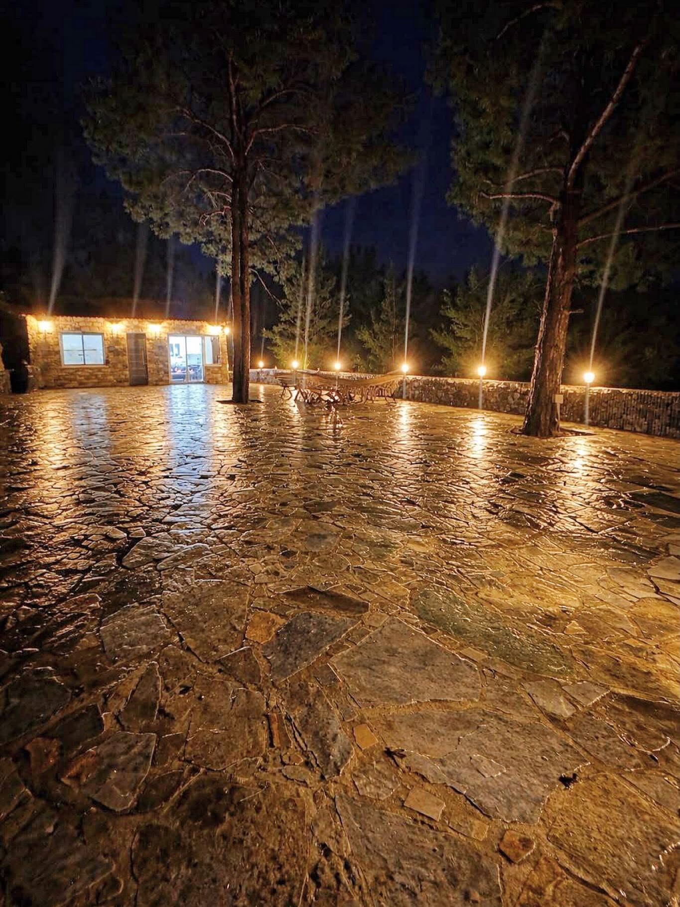The flagstone courtyard at night, lit by wall lights and lantern posts under tall pines